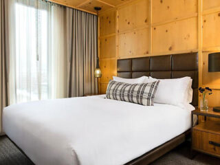 Sleek, modern hotel room with minimalist decor, a large bed, wood paneling, and soft lighting