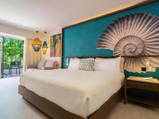 An elegantly designed bedroom featuring a large bed with a teal headboard and seashell artwork.