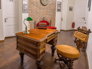 A vintage-inspired office space with a classic wooden desk, green banker's lamp, and plush red chair