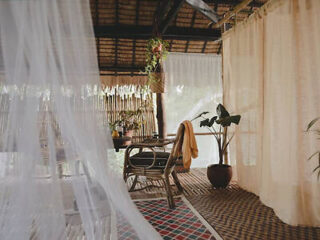 A cozy, rustic reading nook with rattan furniture and sheer curtains, surrounded by lush plants and soft lighting.