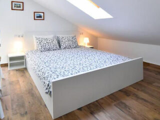 Minimalistic attic bedroom with a large double bed covered in patterned bedding, under a sloped ceiling with skylight windows