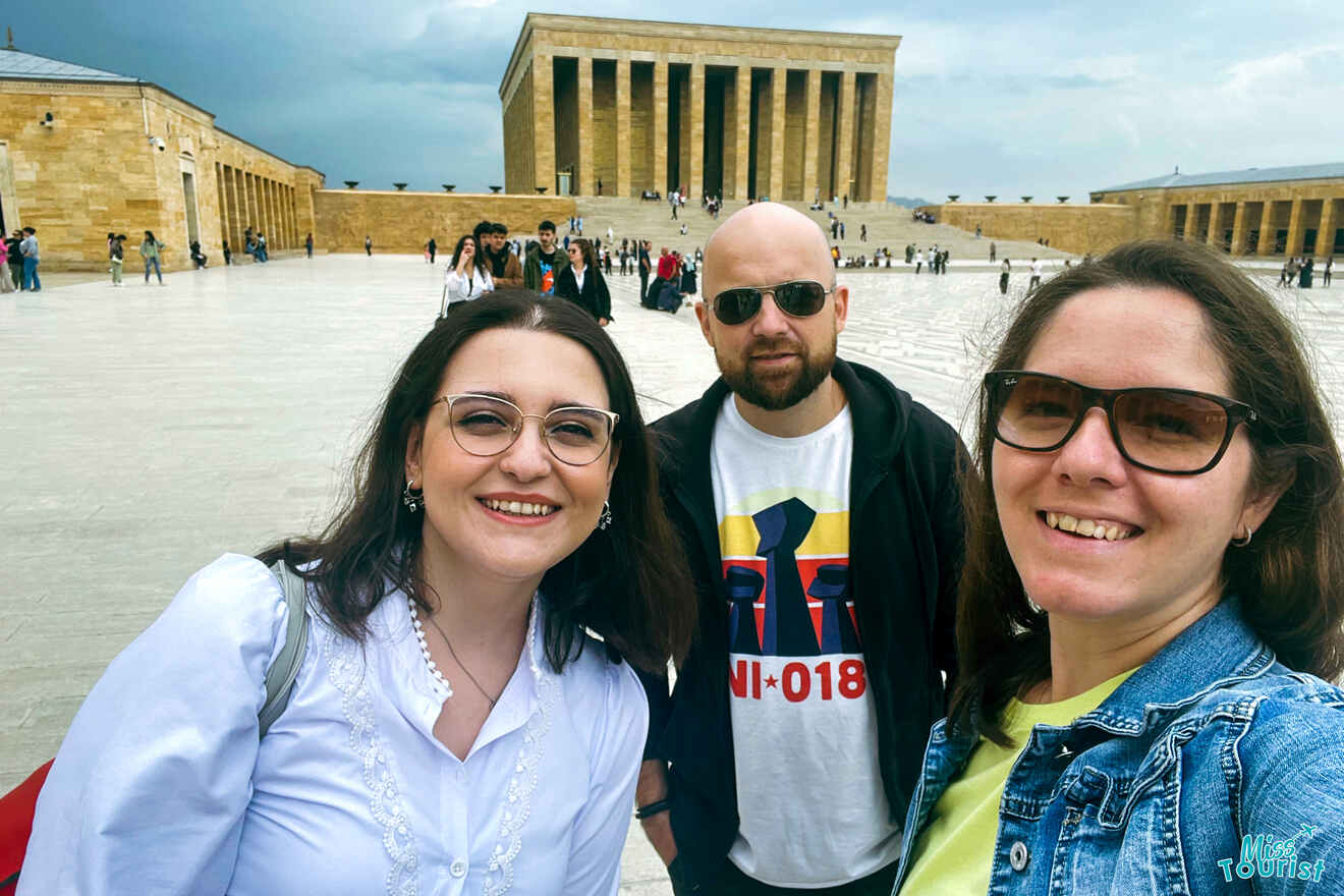 the author of the post with a friend and husband taking a selfie with Anıtkabir, Ataturk's mausoleum, in the background on a cloudy day