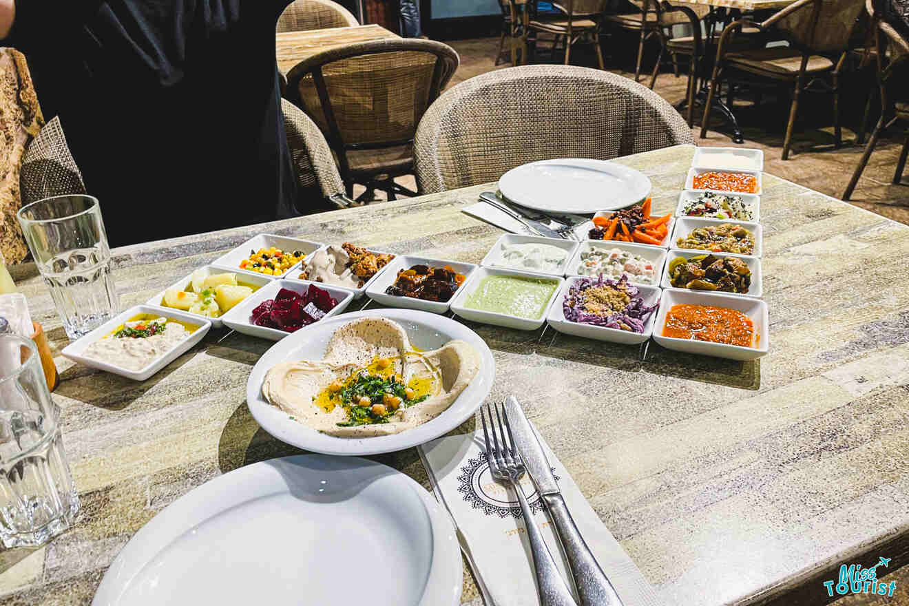 A variety of colorful middle eastern dishes served on a table at a restaurant, including hummus and assorted salads.