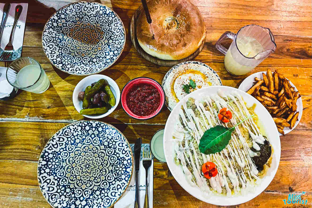 A table set with various dishes including hummus, pita bread, fries, sauces, and decorative plates. drinks are also present.
