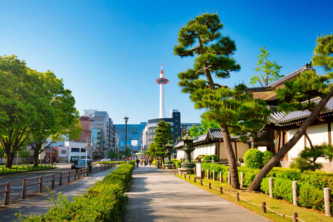 Cityscape with a tree-lined sidewalk, traditional Japanese buildings, and a modern tower in the background on a clear day.