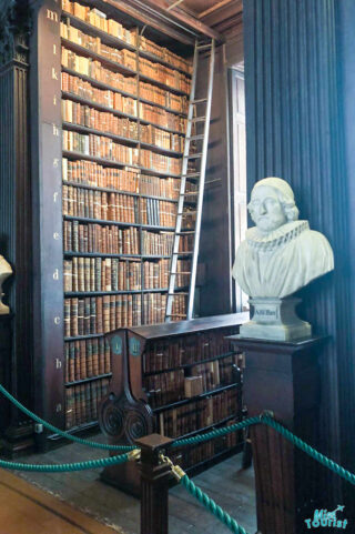 A grand library with a marble bust labeled "ARLbert," a wall of old books, and a sliding ladder.