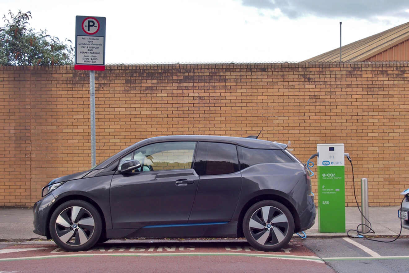 An electric vehicle parked and charging at a public charging station against a brick wall, signifying the growth of eco-friendly transportation options
