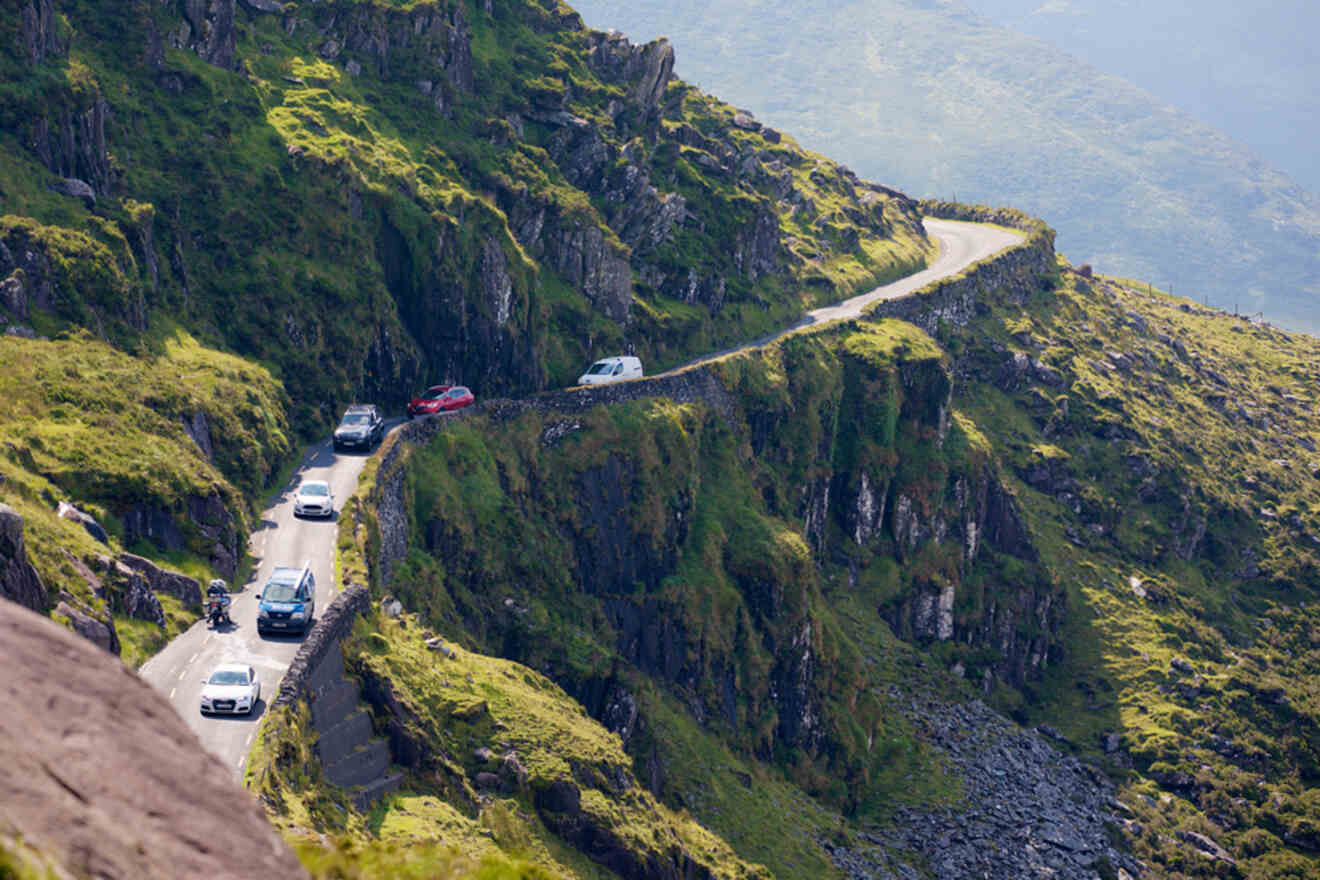 Aerial view of a narrow mountain pass with vehicles navigating the precarious road, showcasing the dramatic landscape and driving conditions in rural Ireland