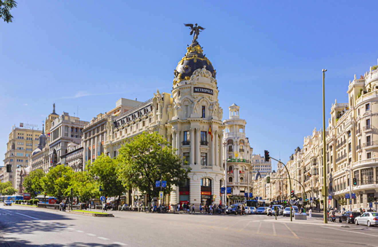The bustling Gran Vía street in Madrid, with historic buildings and the Metropolis Building's distinctive dome and statue