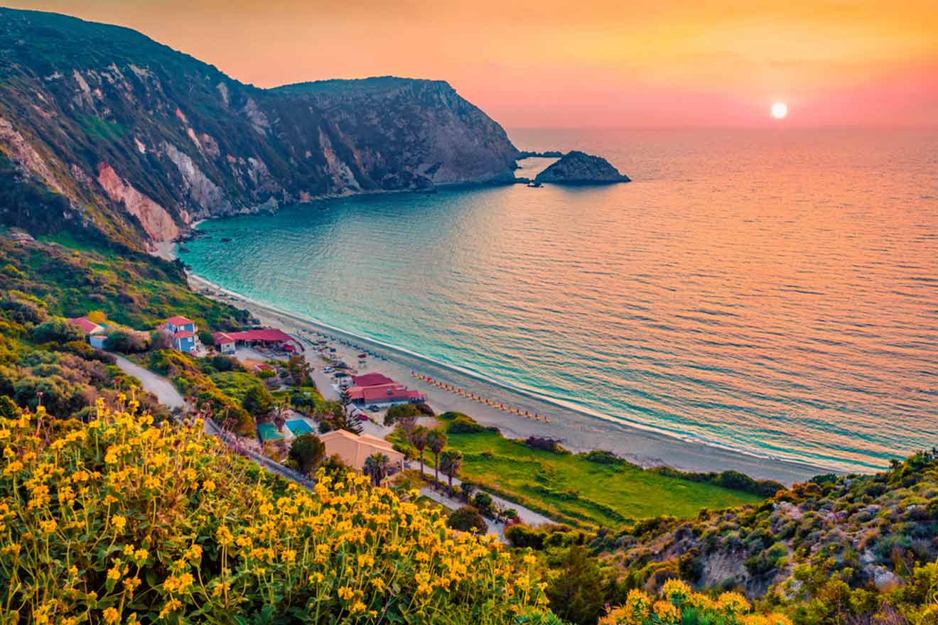 Coastal landscape at sunset with a small village by the sea, surrounded by cliffs and blooming wildflowers.