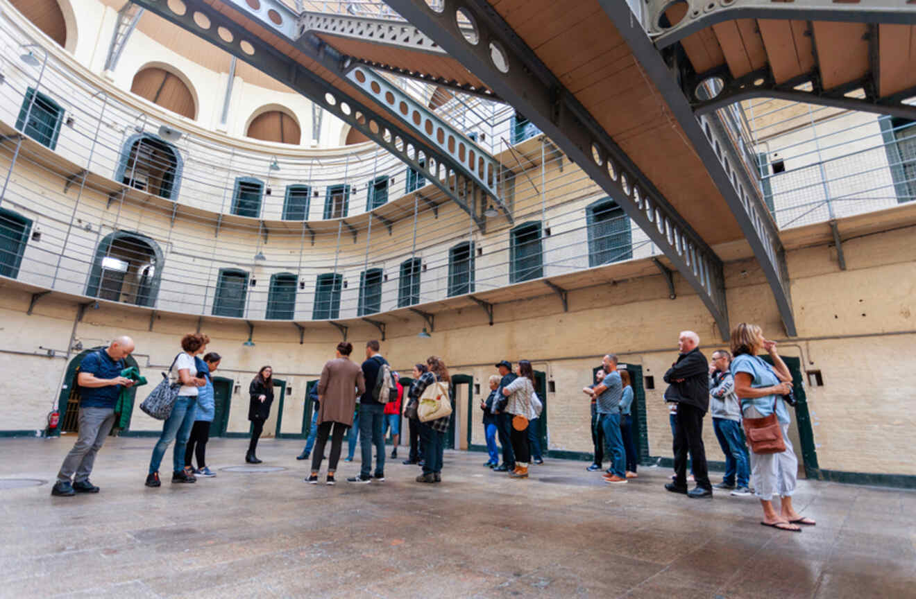 A group of visitors on a guided tour inside the historic Kilmainham Gaol Museum in Dublin, surrounded by the circular cell blocks.