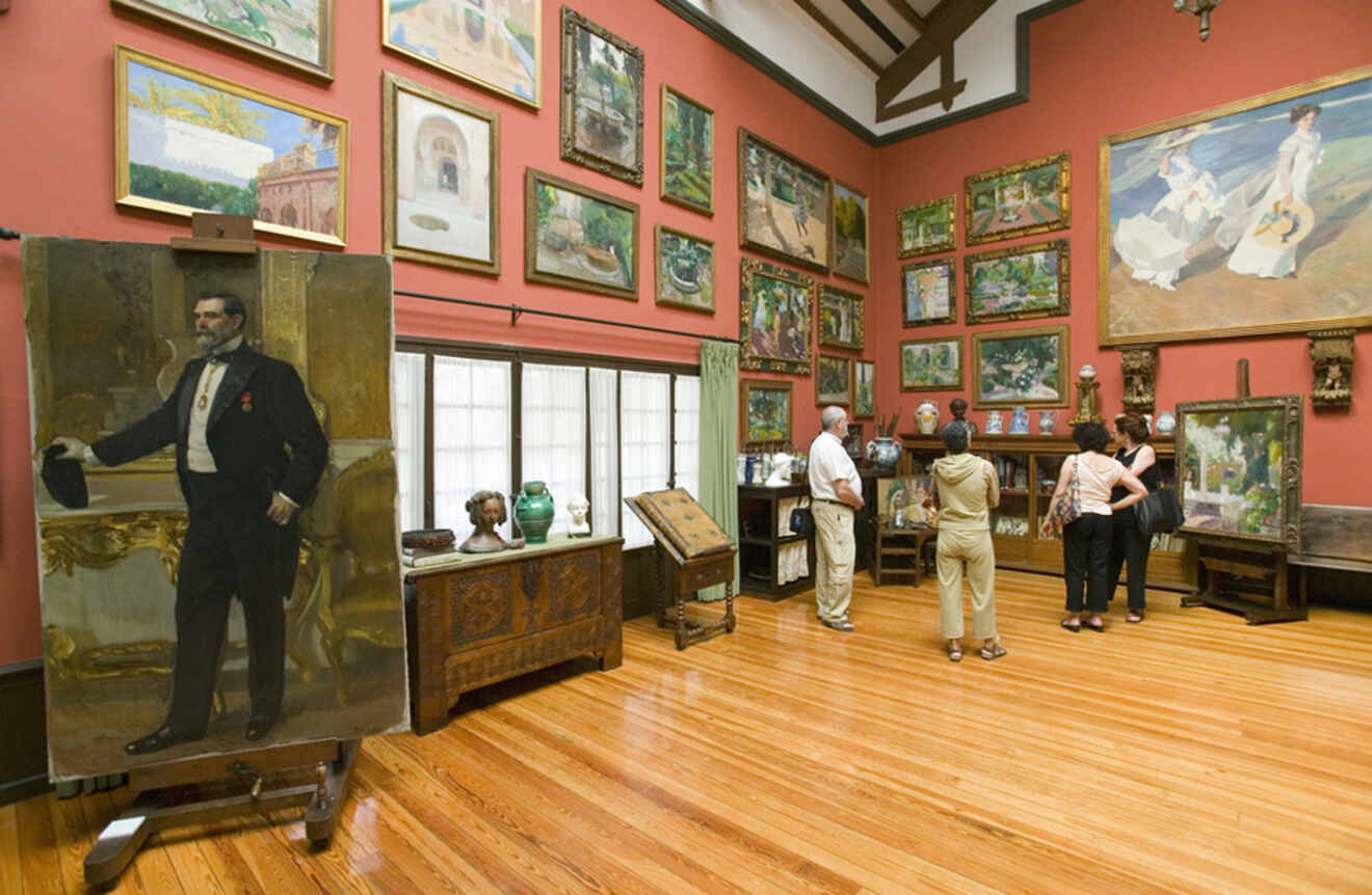 Visitors observing the art collection inside the Sorolla Museum in Madrid, showcasing paintings with richly colored walls and wood accents.