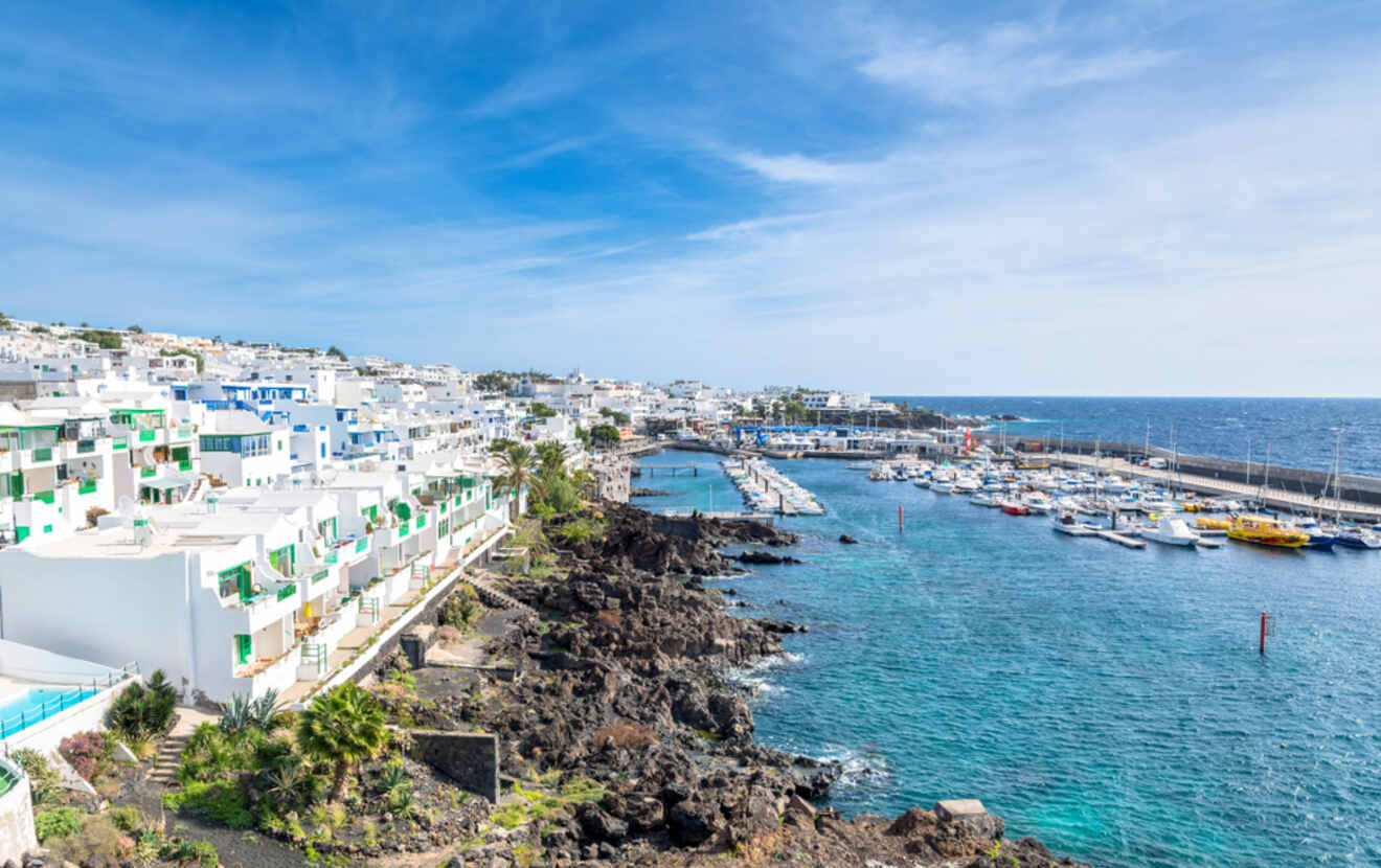 Coastal view of Puerto del Carmen, Lanzarote, displaying the town's white architecture against the backdrop of a bustling harbor and deep blue sea.
