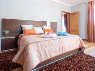 A comfortable bedroom featuring a warm peach-colored bedspread, white and orange cushions, and a textured rust rug