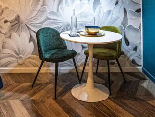 A small modern dining space with a white round table and two plush velvet chairs
