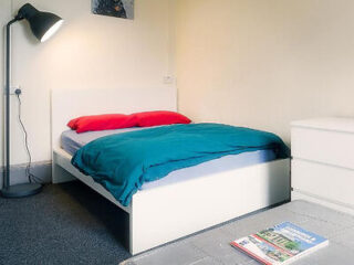 A cozy bedroom with a double bed adorned with red and teal bedding, a floor lamp