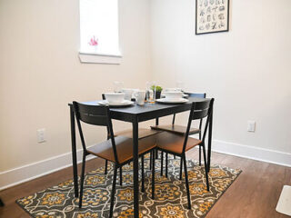 Modest dining area with a small black table set for two, ornamental rug, and framed art