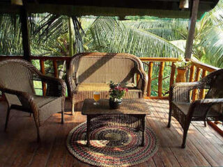 Cozy porch with two wicker chairs and a table, overlooking lush greenery. colorful round rug on wooden floor.