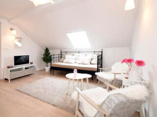 Bright and airy living space with a sofa bed, plush white chairs, a shag rug, and a TV, under a white-pitched ceiling