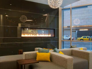 Cozy hotel lobby with a modern fireplace, comfortable seating, and stylish light fixtures, with a view of a city street outside