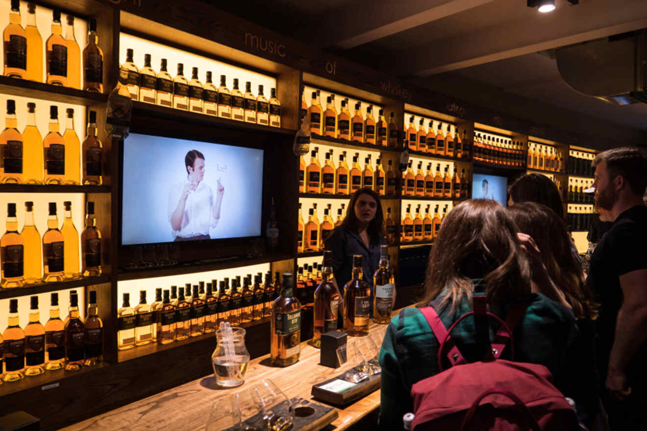 Inside the Irish Whiskey Museum in Dublin, visitors are engaging with an exhibit and whiskey display, with a video presentation in the background.