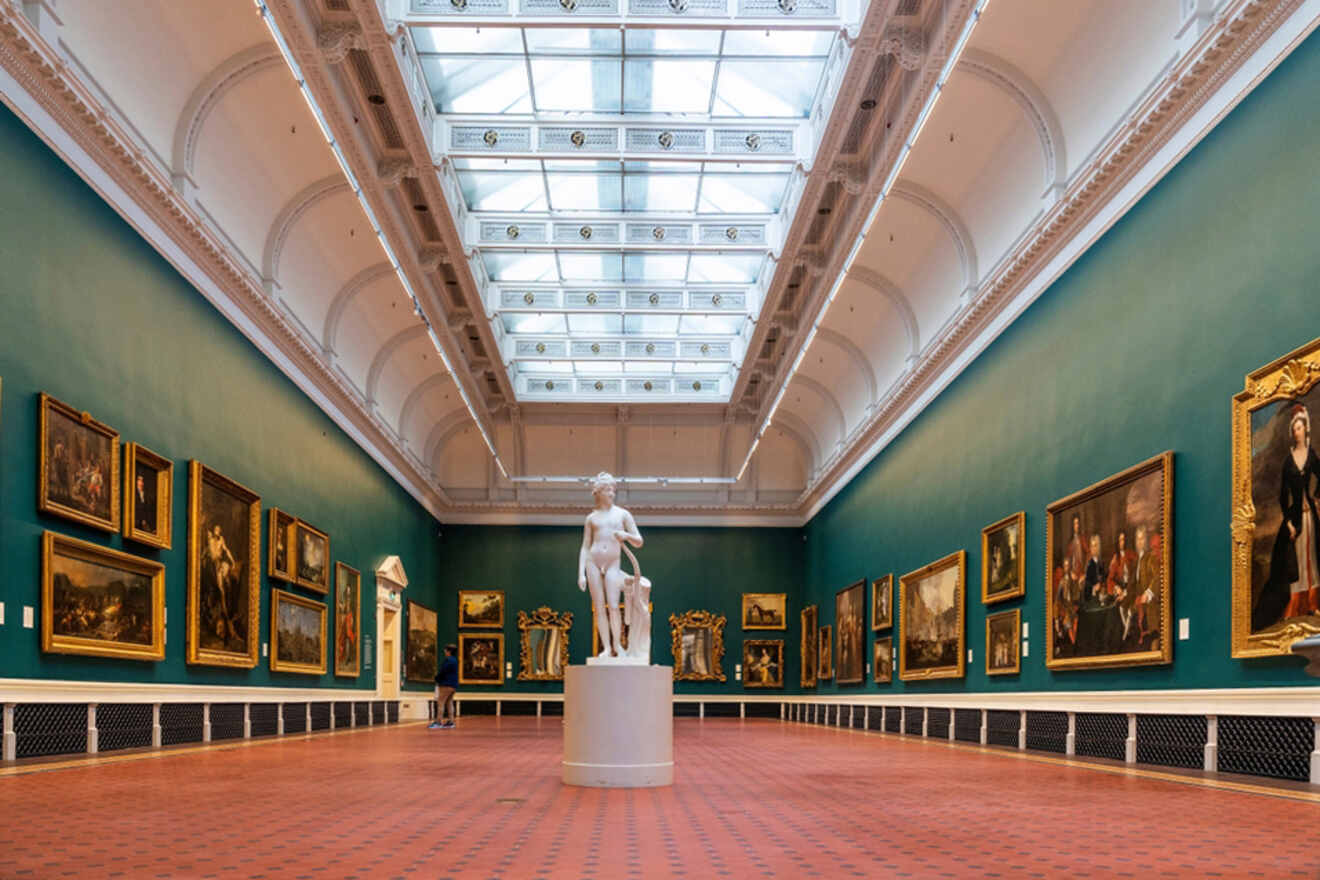 The grand interior of the National Gallery of Ireland in Dublin, showcasing classical artwork, a marble statue in the center, and a glass-paneled ceiling that bathes the space in natural light.