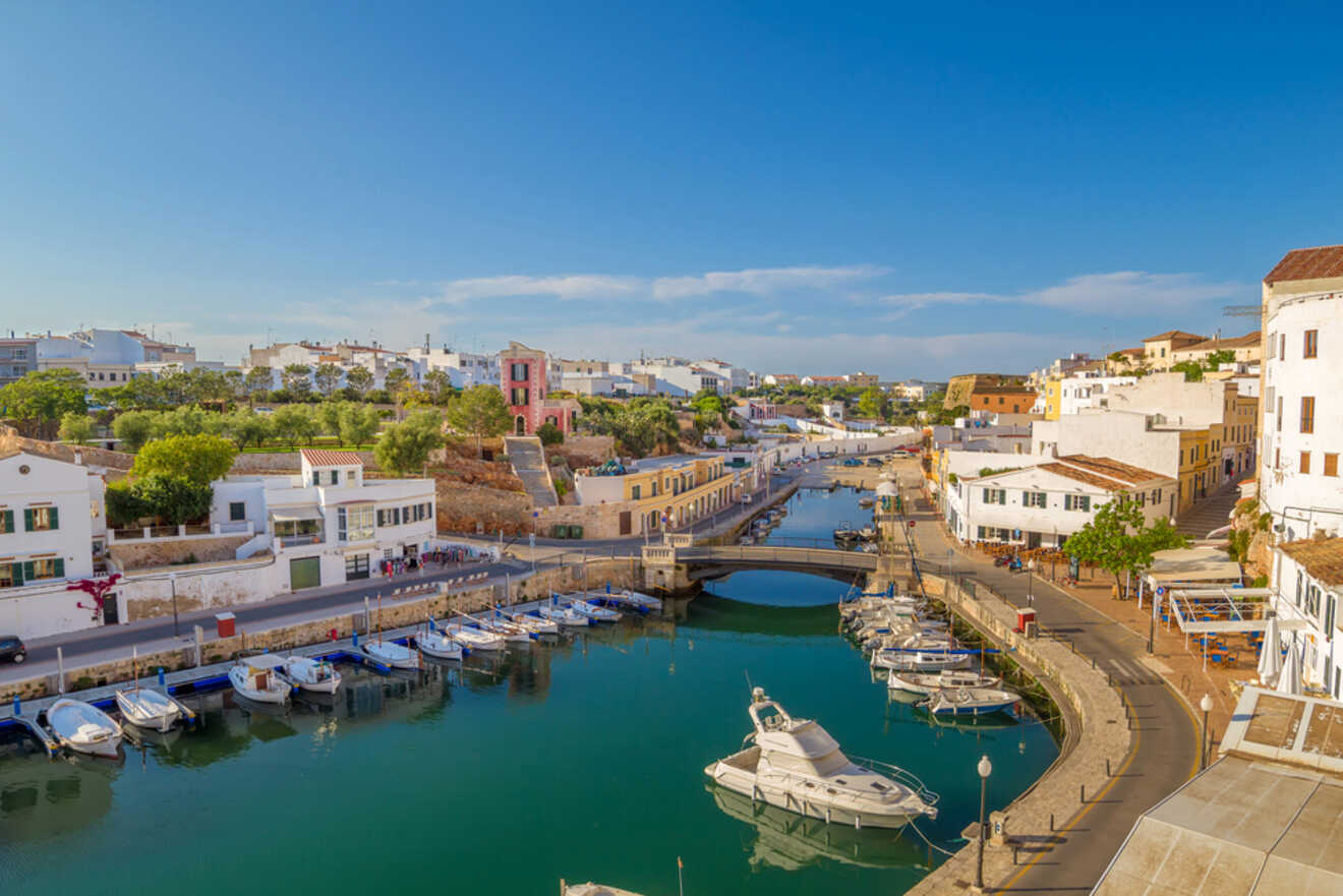 The peaceful harbor of Ciutadella de Menorca, showcasing boats moored in calm blue waters, with a view of the charming waterfront promenade and traditional white buildings