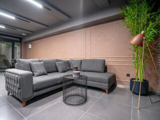 An elegant waiting area with a gray tufted sectional sofa, floor lamp and indoor plants