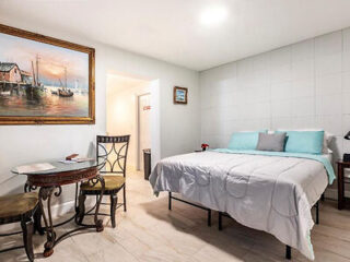 A tidy bedroom with a double bed, a desk with a chair, and a framed painting of boats on the wall.
