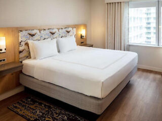 Contemporary hotel bedroom with large bed, abstract art headboard, and wood flooring