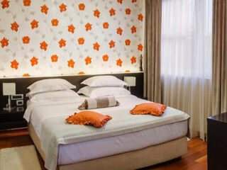 Modern bedroom with a bold orange floral wallpaper, twin beds with matching headboards, and complementary orange cushions