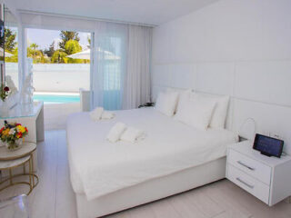Elegant bedroom with a large white bed, clean lines, and a view of the pool