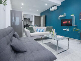 Modern living room with a gray couch, blue accent wall with Netflix logo, and chic decor