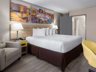 hotel room with a large bed, bright yellow armchair, and wall art of Las Vegas.