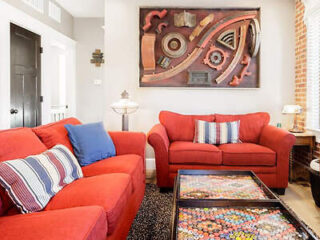 Inviting living room with vibrant red sofas, eclectic wall art, and a unique coffee table filled with colorful marble