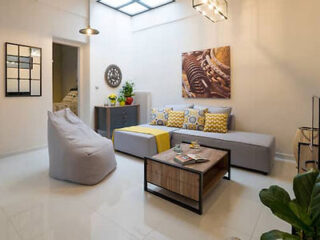 A modern living room featuring a sectional sofa with yellow cushions, a bean bag, a coffee table, and decorative wall art, illuminated by natural light from a skylight.