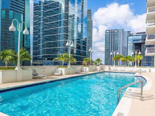 Urban hotel pool deck with cityscape view, lounge chairs, and clear blue water