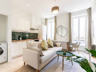 A bright open-plan living area with a contemporary kitchen, light gray sofa, and round coffee table