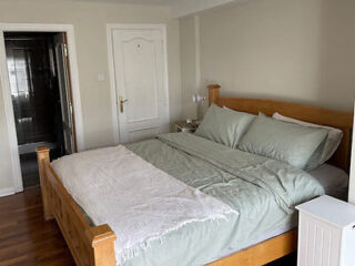 A spacious bedroom featuring a large wooden bed with green sheets, a fluffy gray throw