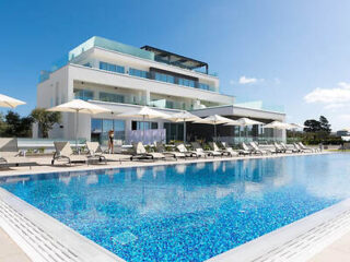 Stylish suites building with a large outdoor swimming pool flanked by white sunbeds and umbrellas