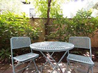 A tranquil garden patio with a metal bistro set surrounded by lush greenery