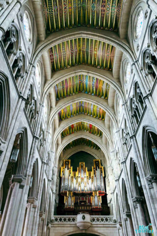 Interior view of the Almudena Cathedral in Madrid, featuring the grand pipe organ, soaring arches, and a stunning, vibrantly colored vaulted ceiling with intricate patterns