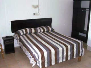A neatly made bed with striped bedding in a simple room with white walls, a black headboard, and minimal furniture.