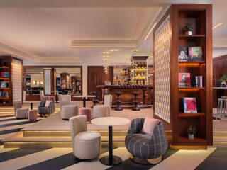 Elegant hotel lobby with plush seating, a wooden bookshelf, and a well-stocked bar in the background.