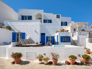 The exterior of a hotel with white-washed walls, blue accents, and a sun-soaked terrace with loungers