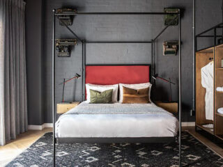 Chic hotel room with a red headboard, industrial style bedside lamps, and an open wardrobe