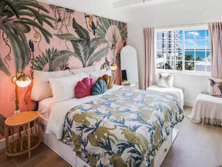 Vibrant beach suite with a botanical wallpaper headboard and ocean view window in Miami.