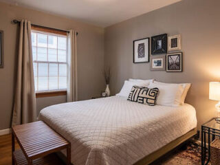 Warmly lit, cozy bedroom with a queen-sized bed covered in a white quilt, flanked by artwork