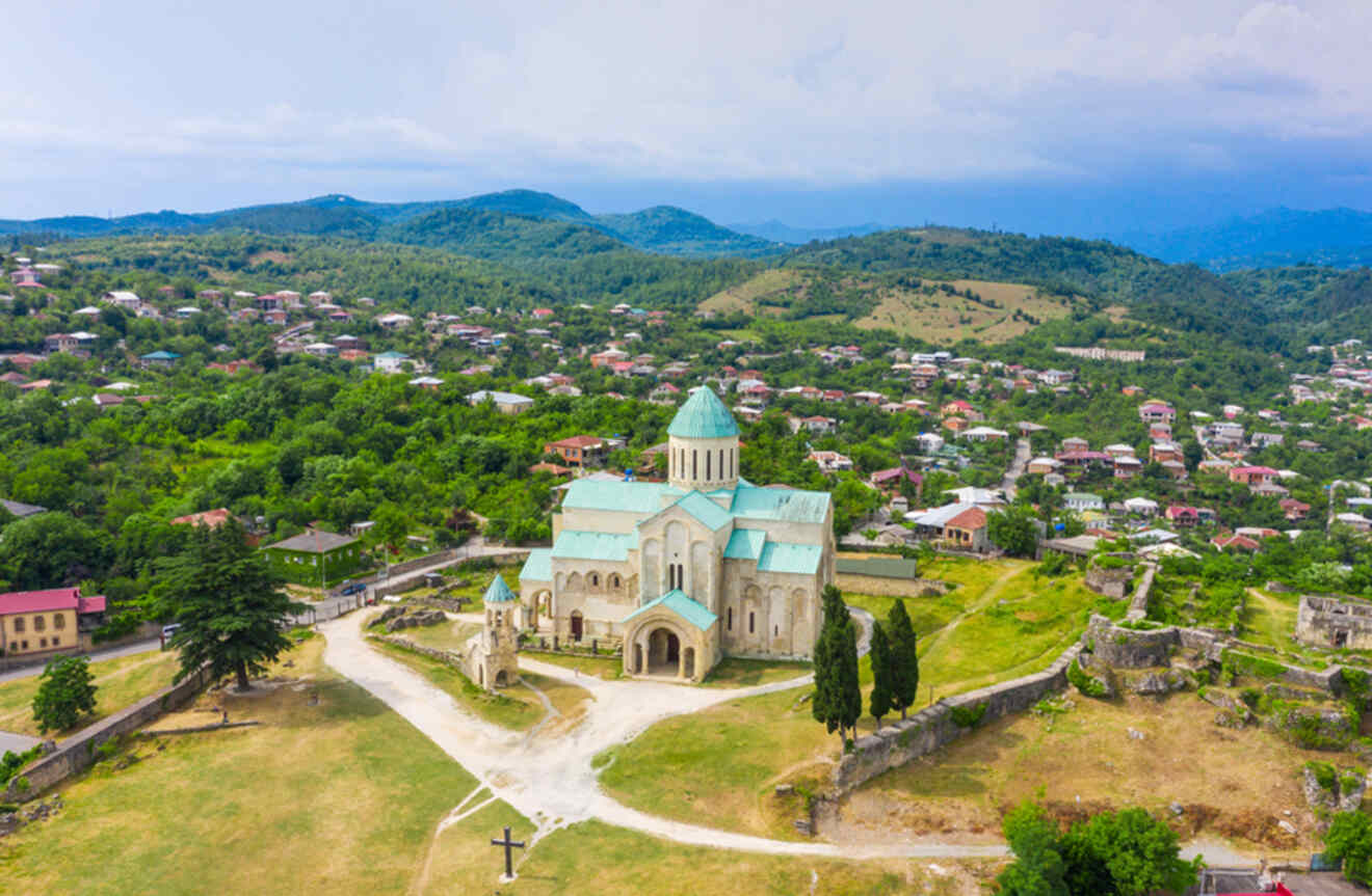 Aerial view of the majestic Bagrati Cathedral in Kutaisi, its stone architecture contrasting with the lush green surroundings and a small town in the distance