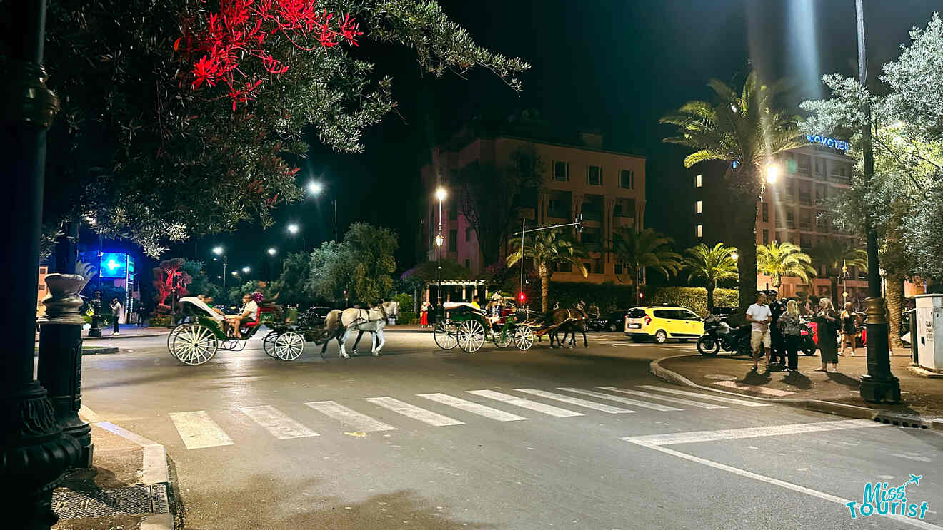 Nighttime street view in Hivernage, Marrakech, with horse-drawn carriages and locals crossing the street, framed by illuminated trees and urban buildings